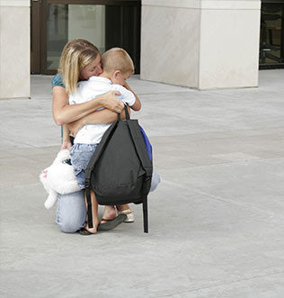 A woman and child hugging on the sidewalk.