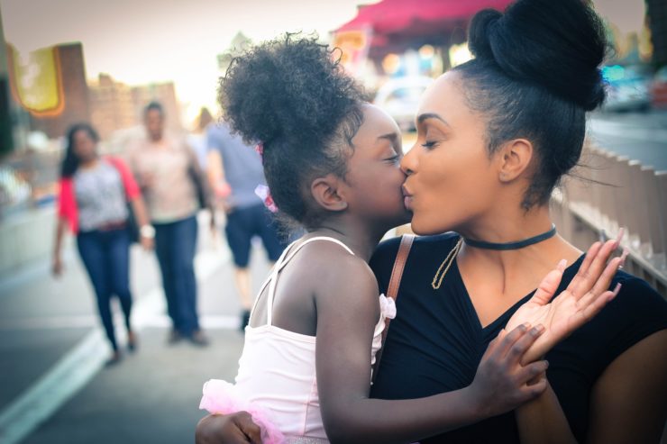 A woman kissing her daughter on the cheek.