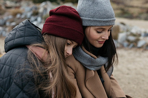 Two women wearing hats and scarves are hugging.