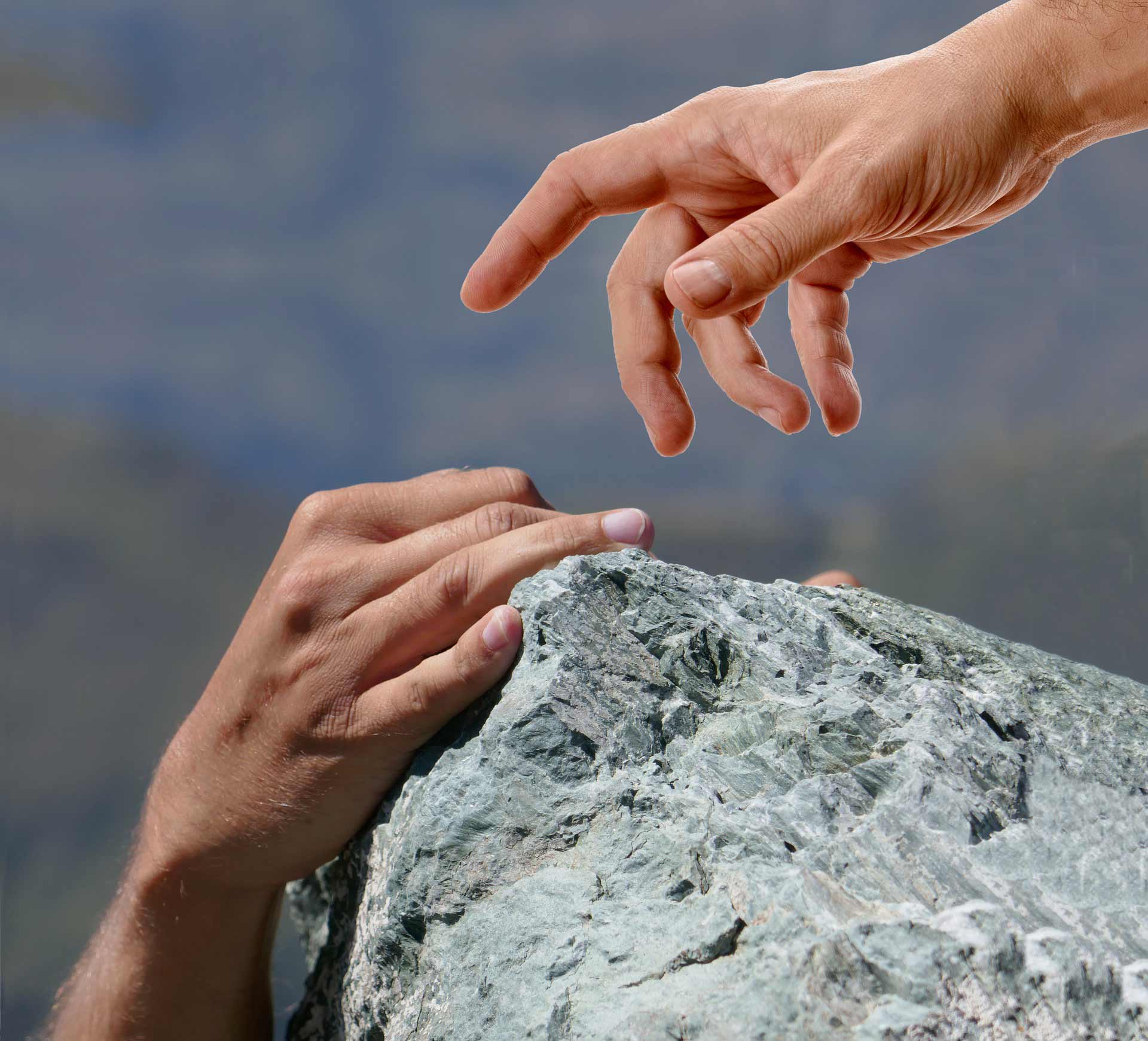 A person reaching out to another person on top of a rock.